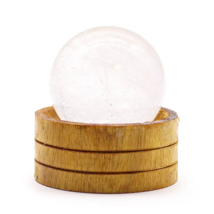 A clear quartz gemstone sphere 50mm rests on a stacked wooden base showing its translucent surface