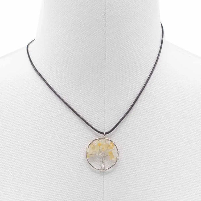 A carnelian gemstone tree of life pendant with yellow crystals in a silver frame hanging from a black cord