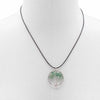 A circular green jade gemstone tree of life pendant on a black cord featuring a gemstone tree design