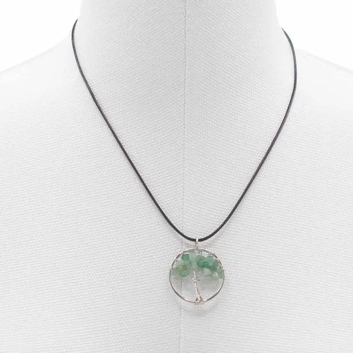 A circular green jade gemstone tree of life pendant on a black cord featuring a gemstone tree design