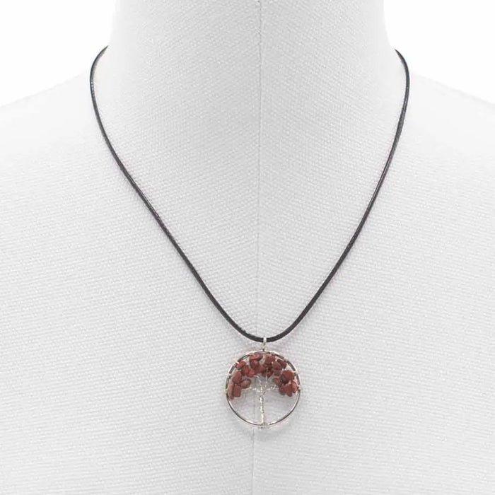 A circular gemstone tree of life pendant with red jasper stones set in a silver-toned frame on a black cord