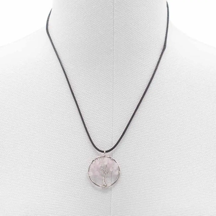 A gemstone tree of life pendant with a translucent pink rose quartz stone and silver wire design on a black cord