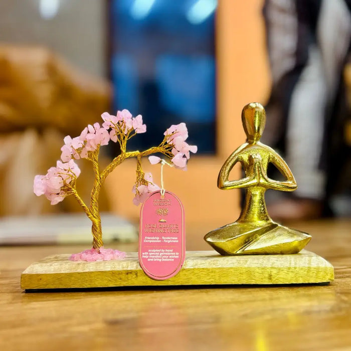 Golden metallic meditation figure in namaste pose seated beside genuine rose quartz tree on mango wood base