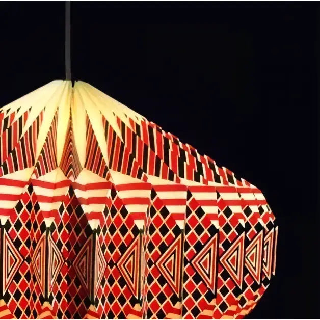 A geometric patterned origami paper pendant lamp with bold red black and cream triangular and diamond motifs