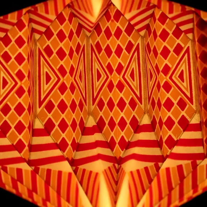 A geometric origami paper lantern light shade with red and orange diamond and striped patterns in bright colors