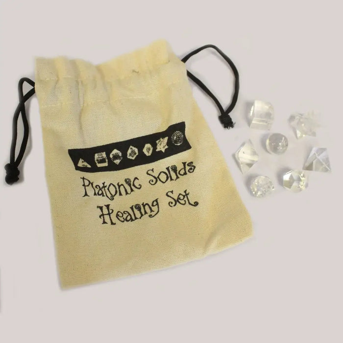 Beige drawstring bag with black embroidery holding a clear quartz seven piece geometric crystal set