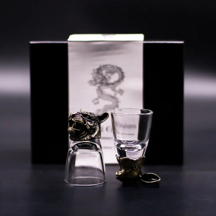 A clear glass shot glass with a golden tiger-head stopper and base from the mystical creatures shot glasses set