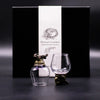 A clear glass decanter with an antique bronze golden dragon stopper and base next to an empty crystal tasting glass