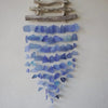 A driftwood wind chime with three sticks made of layered blue sea glass pieces hanging from rustic wood