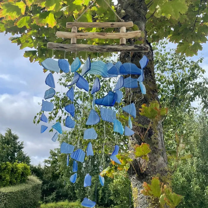 A hanging driftwood wind chime with three rustic wooden sticks and translucent blue glass pieces