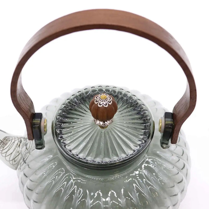 A clear glass infuser teapot with a charcoal ribbed body and wooden handle for brewing tea at home