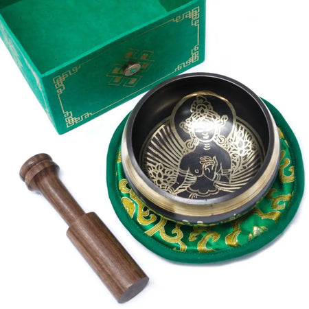 A black and gold green tara singing bowl with engraved buddha design resting on a green embroidered mat