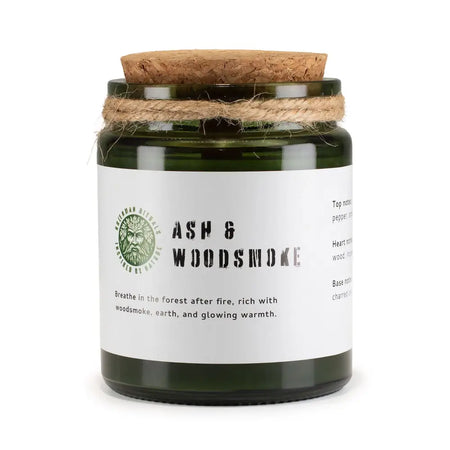 A dark green glass woodwick soy candle with cork lid and twine wrap labeled ash and woodsmoke by greenman naturals