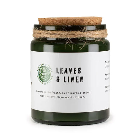 Dark green glass jar woodwick soy candle with cork lid and twine wrap labeled leaves and linen by greenman naturals