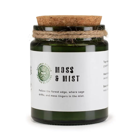 A dark green glass jar woodwick soy candle by greenman woodwick labeled moss and mist with cork lid and twine wrap