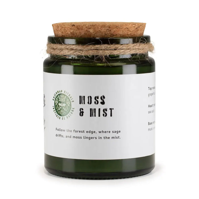 A dark green glass jar woodwick soy candle by greenman woodwick labeled moss and mist with cork lid and twine wrap