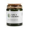A green glass woodwick soy candle with a cork lid and twine wrap labeled sage and mintwood by greenman naturals