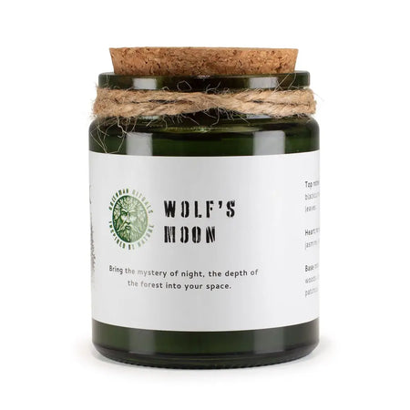 A dark green glass woodwick soy candle jar with cork lid and twine labeled wolf’s moon by greenman rituals
