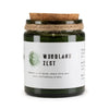 A green glass greenman woodwick soy candle jar with cork lid and twine labeled woodland zest by greenman oils