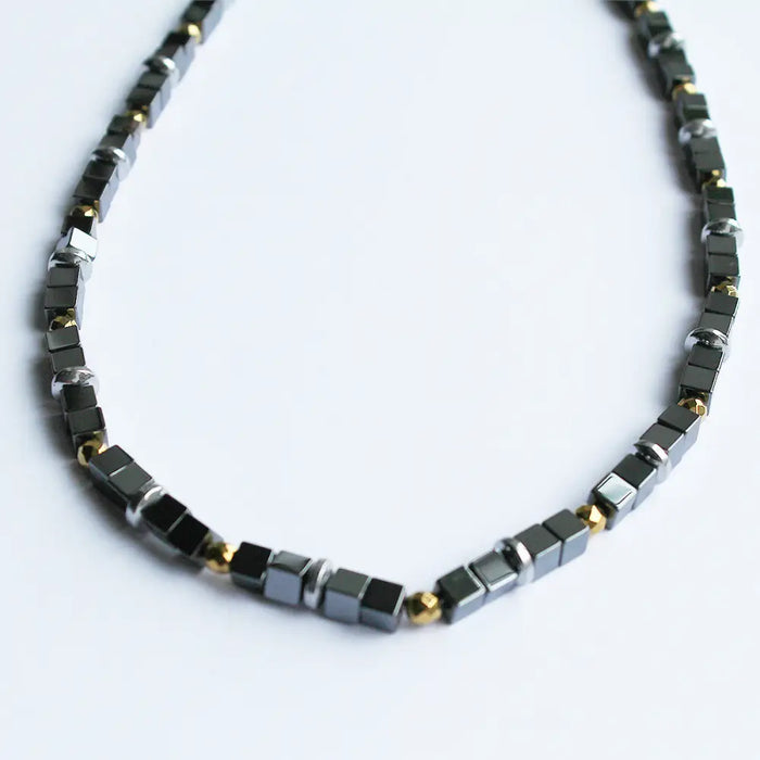 A sleek black and gold finish hematite block beaded necklace with magnetic cube and metallic accents