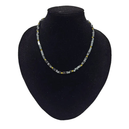 A sleek necklace with gold finish and grey hematite block beads displayed on a black velvet bust