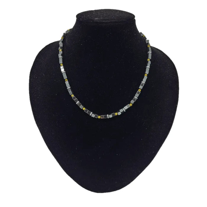 A sleek necklace with gold finish and grey hematite block beads displayed on a black velvet bust