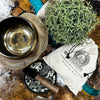 A brass engraved singing bowl with buddha design and tibetan script resting on a wooden base in a bowl gift set