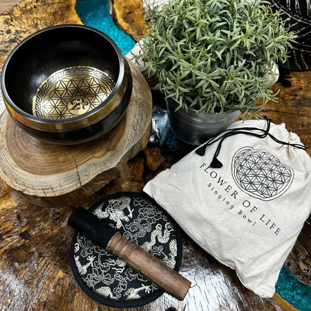 Black hand-beaten engraved singing bowl with gold interior flower of life pattern and mallet on a black base bowl gift set