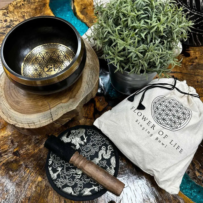 Black hand-beaten engraved singing bowl with gold interior flower of life pattern and mallet on a black base bowl gift set
