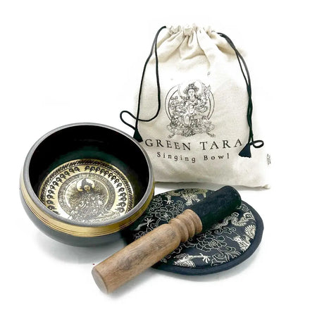 A dark green and gold engraved singing bowl with wooden mallet on an ornate black cushion green tara gift set
