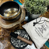 A hand-beaten engraved singing bowl with dark metal exterior and gold lotus flower interior in a singing bowl gift set