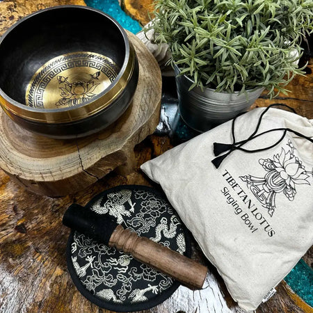 A hand-beaten engraved singing bowl with dark metal exterior and gold lotus flower interior in a singing bowl gift set