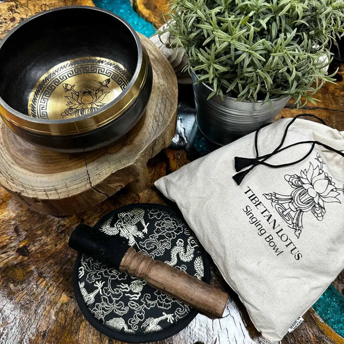 A hand-beaten engraved singing bowl with dark metal exterior and gold lotus flower interior in a singing bowl gift set