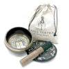Black hand-beaten engraved singing bowl with gold rim and wooden mallet on patterned mat in bowl gift set