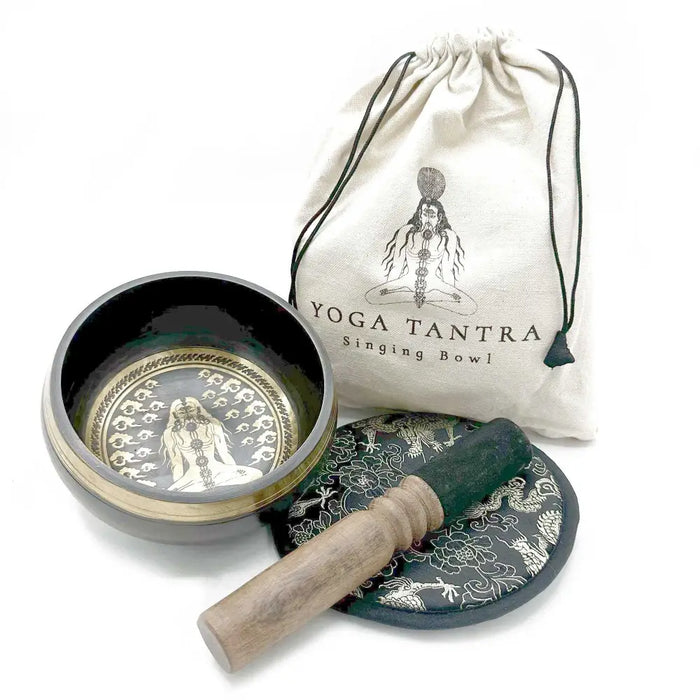 Black hand-beaten engraved singing bowl with gold rim and wooden mallet on patterned mat in bowl gift set