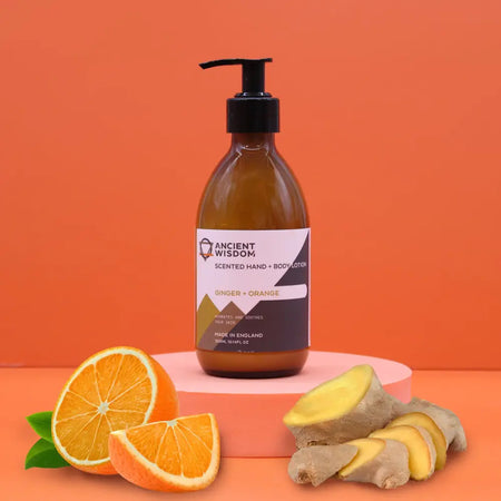 An amber glass bottle of ancient wisdom body lotion with ginger and orange scent on a pink pedestal with black pump