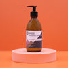 A sleek amber glass bottle of hand and body lotion with black pump in raspberry and pomegranate scent and seed oil