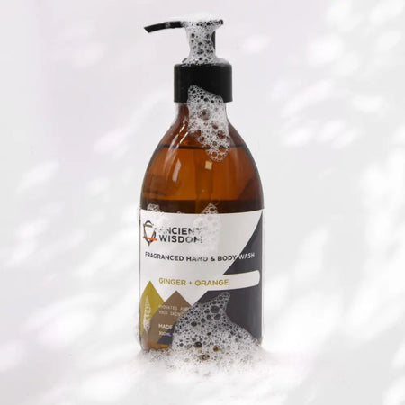 An amber glass bottle of hand and body wash with black pump labeled ginger and orange featuring a fruity scent