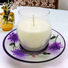 A creamy white scented candle in a clear glass jar on a hand-painted glass candle plate with purple wild flowers