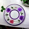 A white ceramic candle plate with a glossy finish featuring hand-painted purple and pink wild flowers and a purple border