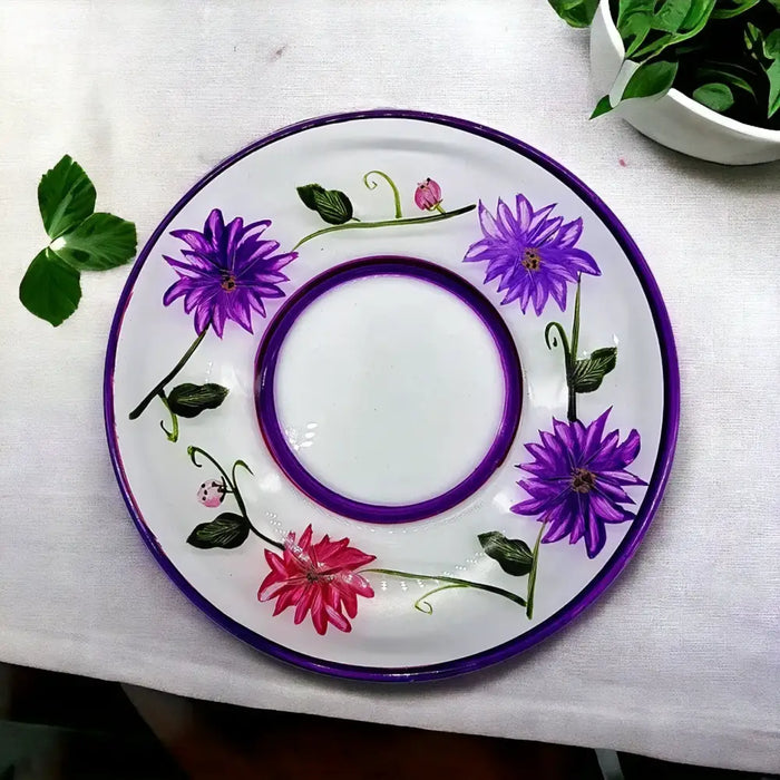 A white ceramic candle plate with a glossy finish featuring hand-painted purple and pink wild flowers and a purple border