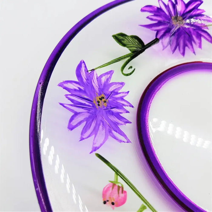 A clear glass candle plate with a purple rim and hand-painted wild flowers including purple and pink blossoms