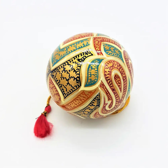 Hand-painted papier maché bauble with cream leaves, gold, teal, and red paisley patterns and a red tassel