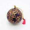 Hand-painted papier maché bauble in purple and gold with cream leaves and a red tassel for christmas decoration