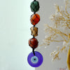 A hanging chakra stone pendant with green, orange, yellow, and red beads in black netting and a purple evil eye charm