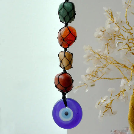 A hanging chakra stone pendant with green, orange, yellow, and red beads in black netting and a purple evil eye charm