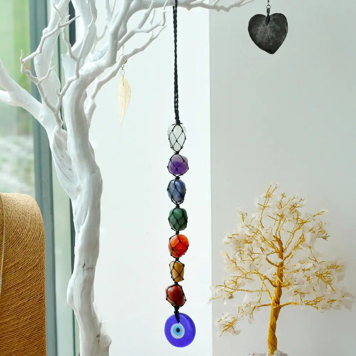 A hanging chakra stone pendant with colorful beads and a blue evil eye on a black cord