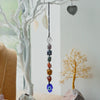 Hanging chakra stone pendant with faceted clear purple blue green orange and red stones on black cord with blue evil eye charm