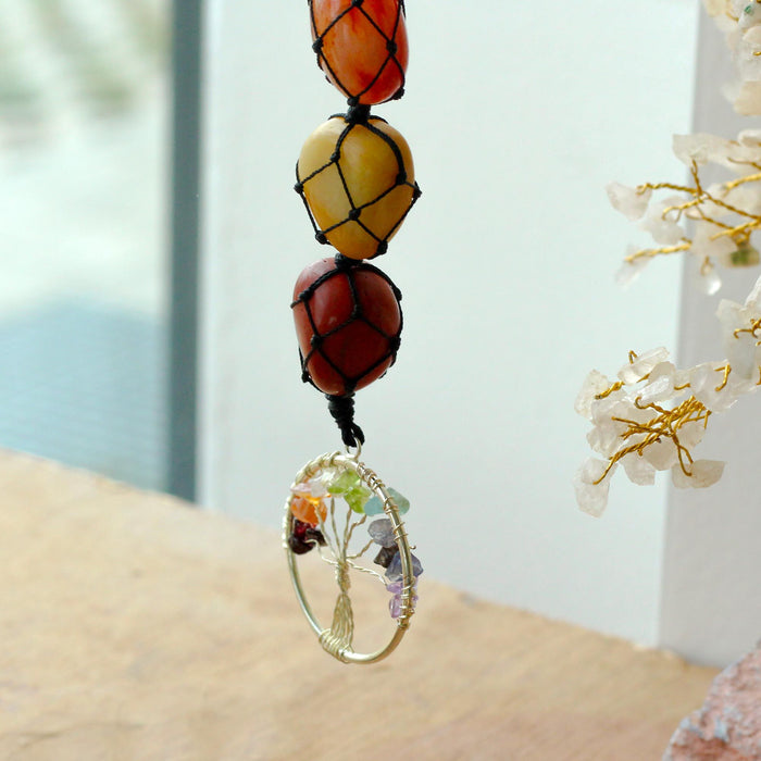 A hanging chakra stone pendant with three colorful netted beads and a wire-wrapped tree of life charm with crystals