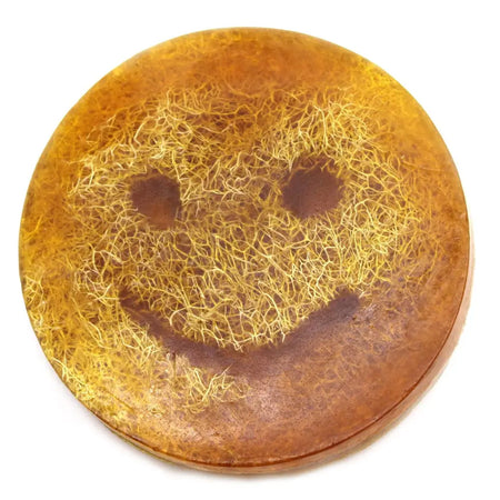 A round amber scrub soap bar with a smiling face design made of golden fibrous material inside